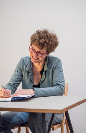 Annette Pehnt lächelnd am Tisch sitzend und Bücher signieren, Foto: Christoph Eberle