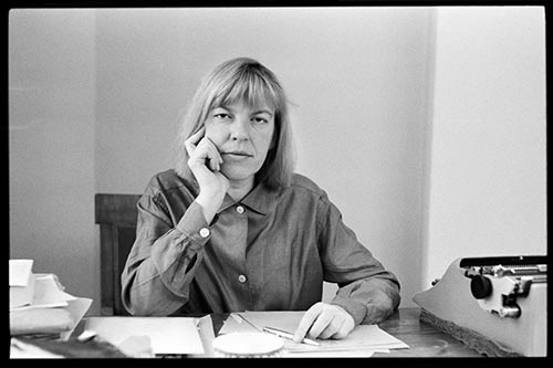 Ingeborg sitzt an einem Tisch mit Stift und Papier und schaut direkt in die Kamera